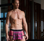A model wearing pink Kinkilt boxer briefs relaxing in a modern living room setting